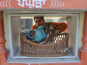 Indian Red Cross Society employee Ashwani Kumar poses with an abandoned baby girl, found at the pictured "pangpura" (cradle) drop off box at the entrance of the Red Cross House in Amritsar on January 21, 2013.