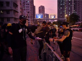 Protesters help each other over barriers in Kowloon Bay in Hong Kong on August 24, 2019, following clashes with police in the latest opposition to a planned extradition law that has since morphed into a wider call for democratic rights in the semi-autonomous city. - Hong Kong riot police on August 24 fired tear gas and baton-charged protesters who retaliated with a barrage of stones, bottles and bamboo poles, as a standoff in a working-class district descended into violence.