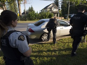 Members of the RCMP Gang Enforcement Team is silhouetted as he speaks to the occupants of a car during a stop in Surrey, B.C., Friday, May 31, 2019.