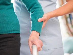 A stock file photo of a senior woman receiving assistance from a health care worker with a walking frame.
