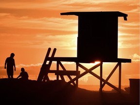 Children play beside a lifeguard tower as sunset approaches at Sunset Beach in Huntington Beach, California.