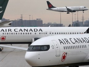 Two Air Canada Boeing 737 MAX 8 aircrafts are seen on the ground as Air Canada Embraer aircraft flies in the background at Toronto Pearson International Airport in Toronto, on March 13, 2019.