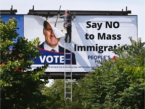 FILE: A worker removes a billboard featuring the portrait of People's Party of Canada (PPC) leader Maxime Bernier and its message "Say NO to Mass Immigration" in Toronto.