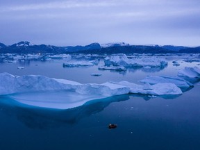 In this Aug. 15, 2019, photo, a boat navigates at night next to large icebergs near the town of Kulusuk, in eastern Greenland. An international scientific body says the damage to earth's oceans and glaciers from climate change is now outpacing the ability of governments to protect them.