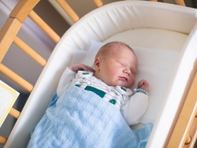 Newborn baby in hospital room. New born child in wooden co-sleeper crib. Infant sleeping in bedside bassinet. Safe co-sleeping in a bed side cot. Little boy taking a nap under knitted blanket.