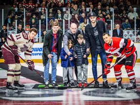 Dave Smart, middle, accompanied by his sons Gabe, middle left, and Theo, middle right, and Carleton Ravens men's basketball team members Mitch Wood, left, and Mitch Jackson, right, performs a ceremonial faceoff before the Ontario Hockey League game between the Peterborough Petes and Ottawa 67's at TD Place arena on March 15.