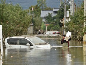 A man wades through floodwaters with items salvaged from his home in the aftermath of Typhoon Hagibis in Nagano on Monday. Tens of thousands of rescue workers were searching for survivors two days after the storm slammed into Japan, killing at least 35 people.