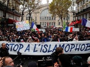 People wave French national flags, chant slogans and hold placards reading messages such as "Stop to all types of racism" (rear L) and "Stop to Islamophobia" (front C) as they take part in a demonstration march in front of the Gare du Nord, in Paris to protest against Islamophobia, on November 10, 2019.