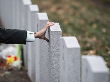 A member of the Canadian Forces touches the crest on a tombstone at the National Military Cemetery at Beechwood Cemetery following a Remembrance Day ceremony in Ottawa, on Monday, Nov. 11, 2019.