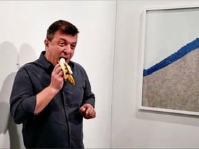 David Datuna eats a banana that was attached with duct tape to a wall, which was an artwork titled 'Comedian' by the artist Maurizio Cattelan, in front of a crowd at Art Basel in Miami Beach, Florida, U.S., December 7, 2019, in this still image from video obtained via social media