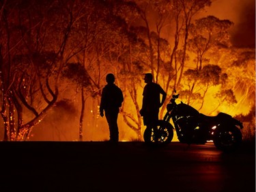 Residents look on as flames burn through bush on January 04, 2020 in Lake Tabourie, Australia.