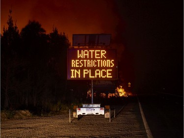 A sign displaying a "Water Restriction" message is pictured as flames burn in the background on January 04, 2020 in Lake Tabourie, Australia. A state of emergency has been declared across NSW with dangerous fire conditions forecast for Saturday, as more than 140 bushfires continue to burn. There have been eight confirmed deaths in NSW since Monday 30 December. 1365 homes have been lost, while 3.6 million hectares have been burnt this fire season.