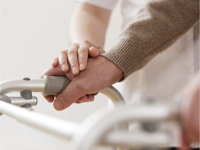 A physiotherapist supports a disabled senior man with a walker.