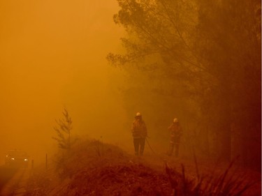 Firefighters tackle a bushfire in thick smoke in the town of Moruya, south of Batemans Bay, in New South Wales on January 4, 2020. - Up to 3,000 military reservists were called up to tackle Australia's relentless bushfire crisis on January 4, as tens of thousands of residents fled their homes amid catastrophic conditions.