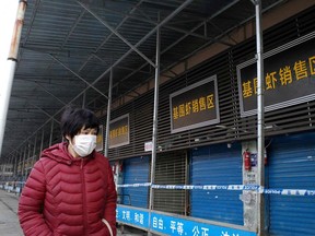 A woman walks in front of the closed Huanan wholesale seafood market, where health authorities say a man who died from a respiratory illness had purchased goods from, in the city of Wuhan, Hubei province, on Sunday. A 61-year-old man has become the first person to die in China from a respiratory illness believed caused by a new virus from the same family as SARS, which claimed hundreds of lives more than a decade ago, authorities said.