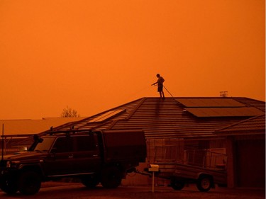 A resident uses a garden hose to wet down the house as high winds push smoke and ash from the Currowan Fire towards Nowra, New South Wales, Australia January 4, 2020.