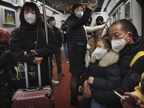 A Chinese man holds a child as they and others wear protective masks while riding on the subway on Jan. 24, 2020, in Beijing, China.