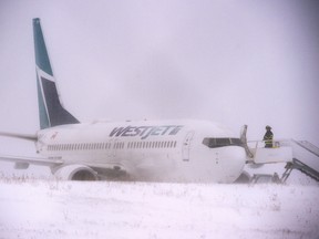 A firefighter stands on the steps of a Westjet aircraft that skidded off the runway at Halifax Stanfield International Airport on Sunday, Jan. 5, 2020. (THE CANADIAN PRESS/Andrew Vaughan)