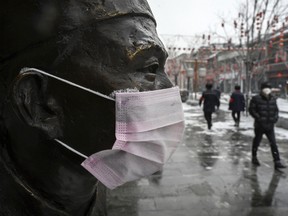 A protective mask is seen on a statue outside a restaurant as people walk by in an empty and shuttered commercial street on February 5, 2020 in Beijing, China.