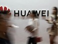 In this file photo taken on August 2, 2019 people walk past a Huawei logo during the Consumer Electronics Expo in Beijing.