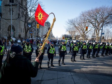 A man carrying a Mohawk Warrior Flag faces a line of Parliamentary Protective Service officers during the All Eyes on Parliament: Rally for the Wet'suwet'en in downtown Ottawa. February 24, 2020.