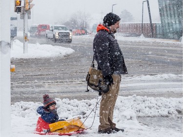 A man and young child wait to cross Scott Street at Holland Avenue during a heavy snowfall in Ottawa.