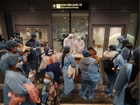 Officials (C) check details of Vietnamese citizens repatriated from Wuhan, where the SARS-like novel coronavirus originated, upon their arrival at the Van Don airport in Vietnam's  Quang Ninh province on Monday.