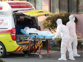 Medical workers wearing protective gear transfer a suspected coronavirus patient (L) to another hospital from Daenam Hospital where a total of 16 infections have now been identified with the COVID-19 coronavirus, in Cheongdo county near the southeastern city of Daegu on February 21, 2020.