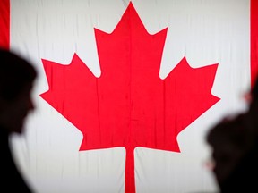 People silhouetted in front of the Canadian national flag.