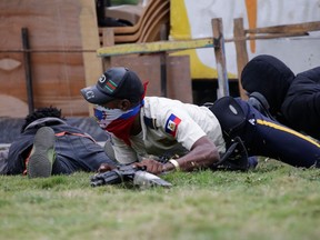 A masked man in a Haitian National Police uniform crawls on the ground during a shooting in Champ de Mars, Port-au-Prince, Haiti on Sunday.
