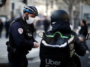 A French police officer checks a motorist in Belleville neighborhood as a lockdown imposed to slow the rate of the coronavirus disease (COVID-19) contagion started at midday in all the country, in Paris, France on Monday.