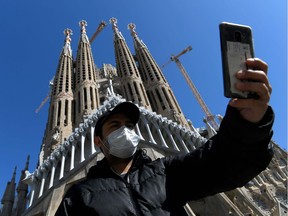 A tourist wearing a protective mask takes a selfie outside the Sagrada Familia in Barcelona on March 11, 2020.