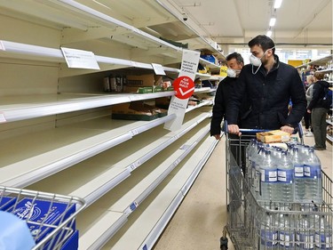 Shoppers wearing masks are faced with partially empty shelves at a supermarket in London on March 14, 2020, as consumers worry about product shortages, leading to the stockpiling of household products due to the outbreak of the novel coronavirus COVID-19.