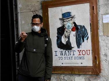 A man wearing a face mask poses with a poster by artist TVBoy featuring Uncle Sam and reading "I want you to stay home" in Barcelona on March 14, 2020 after regional authorities ordered all shops in the region be shuttered from today through March 26, save for those selling food, chemists and petrol stations, in order to slow the coronavirus spread.