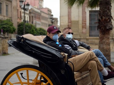 Two tourists wearing protective masks drive along a street on a buggy in Seville, on March 14, 2020. - Seville decided today to cancel its famous Holy Week processions, scheduled for April 5 to 12, due to the spread of the novel coronavirus, COVID-19, in Spain, local authorities announced.
