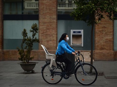 A woman wearing a protective mask rides her bike along a street in Seville, on March 14, 2020. - Seville decided today to cancel its famous Holy Week processions, scheduled for April 5 to 12, due to the spread of the novel coronavirus, COVID-19, in Spain, local authorities announced.
