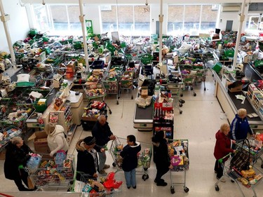 Trolleys piled high for delivery are seen as shoppers queue at the checkout of a supermarket in London on March 14, 2020, as consumers worry about product shortages, leading to the stockpiling of household products due to the outbreak of the novel coronavirus COVID-19.