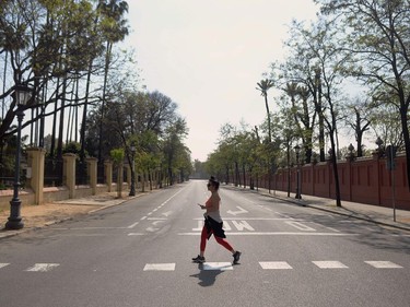 A woman crosses an empty avenue in Seville, on March 14, 2020. - Seville decided today to cancel its famous Holy Week processions, scheduled for April 5 to 12, due to the spread of the novel coronavirus, COVID-19, in Spain, local authorities announced.