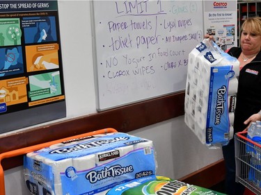 An employee loads products onto a cart in front of signs about Covid 19 and the rationing of products for sale at a Costco store in Novato, California on March 14, 2020. - Hoards of shoppers rushed to stock up on toilet paper, paper towels and cleaning supplies as communities begin hunkering down as a result of the Coronavirus.