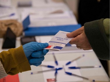 An electoral officer wearing plastic gloves holds an electoral card on March 15, 2020, at a polling station in Mulhouse, eastern France, during the first round of mayoral elections in France, as France battling the coronavirus that causes the COVID-19 disease. - Officials have been told to disinfect voting booths and ballot boxes throughout the day, and sinks and hand gels will be made available. People will be urged to get in and out quickly to avoid lines, and floor markings will be laid out to ensure they stay one metre (3.3 feet) from one another. Authorities have already eased proxy voting rules for people at risk or infected with coronavirus and ordered to confine themselves to their homes, as well as for people in retirement homes. People can also come with their own pens for marking ballots.