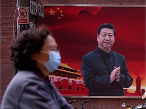 A woman wearing a protective mask moves past a portrait of Chinese President Xi Jinping on a Shanghai street March 12.