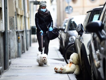 A woman wearing a face mask and gloves walks a dog as a teddy bear is seen on a sidewalk, on the sixth day of an unprecedented lockdown across of all Italy imposed to slow the outbreak of coronavirus, in Turin, Italy, March 15, 2020.