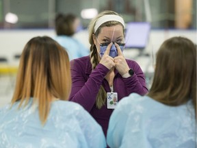 A nurse demonstrates to others how to wear a face mask.