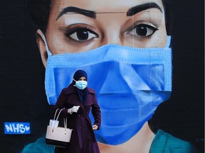 A woman wearing a face mask walks past a piece of street art depicting an NHS worker on April 21, 2020 in the Shoreditch area of London, England.