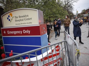Pedestrians wearing personal protective equipment due to COVID-19 concerns gather to applaud medical workers at Brooklyn Hospital Center, Tuesday, April 14, 2020, in New York.