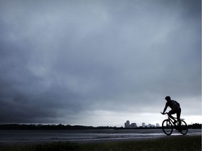 A cyclist rolls along with dark clouds rolling in overhead.