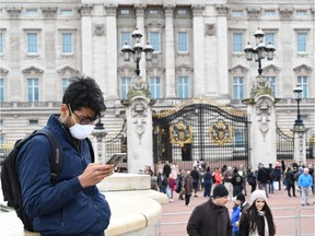 A tourist wearing a mask checks his cellphone in front of Buckingham Palace in London in early March.