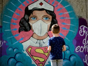 A boy stands in front of a graffiti painted by artist Kai 'Uzey' Wohlgemuth featuring a nurse as Superwoman on a wall in Hamm, western Germany, on April 8, 2020.