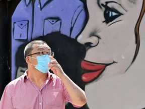 A face mask-clad pedestrian is seen by a mural as he waits to cross a road in the Burwood suburb of Sydney on April 14, 2020, amid the COVID-19 coronavirus pandemic.