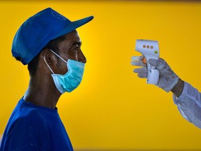 A resident living close to a boarding house, which housed foreign students from Malaysia, gets his temperature taken by an Indonesian health officer amid the COVID-19 coronavirus pandemic in Banda Aceh on April 20, 2020.